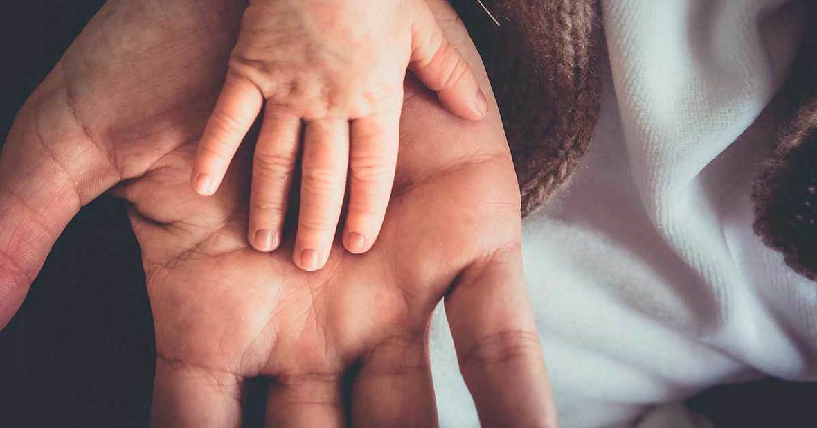 Mano de un niño pequeño sobre la de un adulto enfermo de alzhéimer