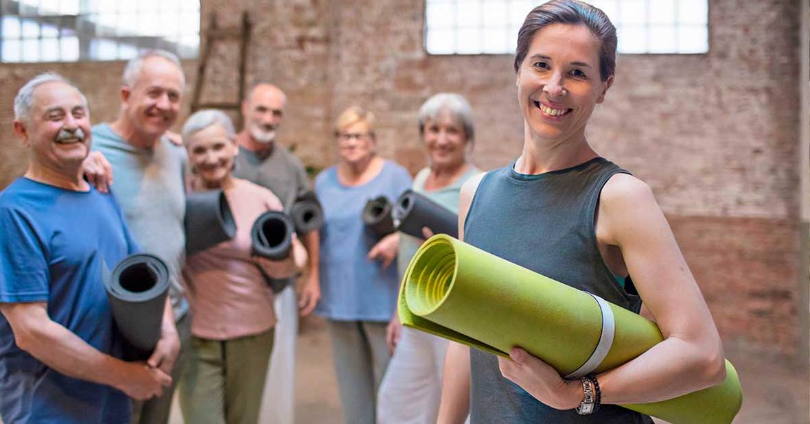 Grupo de clase de yoga, una buena forma de mantenerse activo en la tercera edad, con la profesora y varias personas mayores sujetando sus esterillas