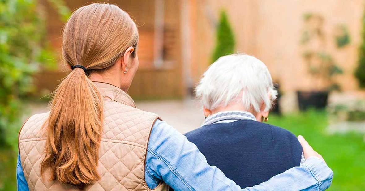 Mujer joven acompañando a una anciana enferma de alzhéimer, ayudándola a caminar con un brazo en sus hombros