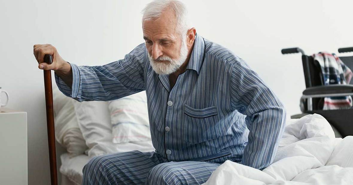Persona mayor intentando levantarse de la cama mientras se ayuda de un bastón para incorporarse