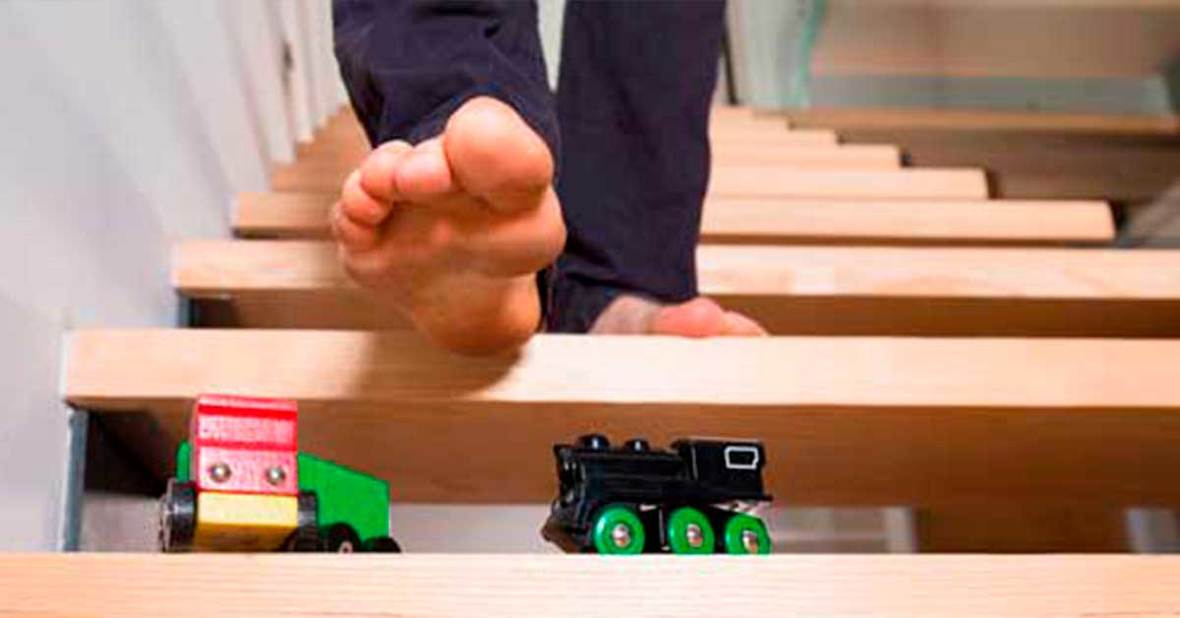 Persona bajando por una escalera y a punto de pisar unos coches de juguetes colocados en un escalón, una situación que debe evitarse al cuidar de una persona mayor